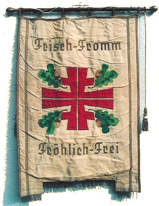 Banner des Turngaues Rhein-Lahn. Das Bild zeigt eine Fahne in der Grundfarbe hellbeige. In der Mitte ist in roten Buchstaben das sog. Turnerkreuz, bestehend aus vier großen "F" abgebildet, außerdem vier Eichenblätter mit Eicheln. Eingerahmt ist alles mit dem Wahlspruch der Turnerschaft: "Frisch, Fromm, Fröhlich, Frei". Das Banner ist an der Oberseite an einer verzierten Holzstange aufgehängt, am rechten Rand hängt eine goldene Zierkordel mit Quaste.